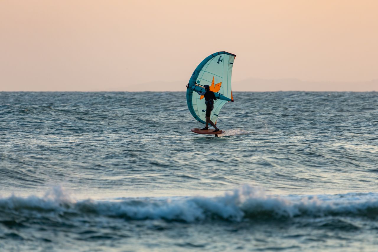 Kitesurfer skillfully riding the waves at sunset in the open ocean.